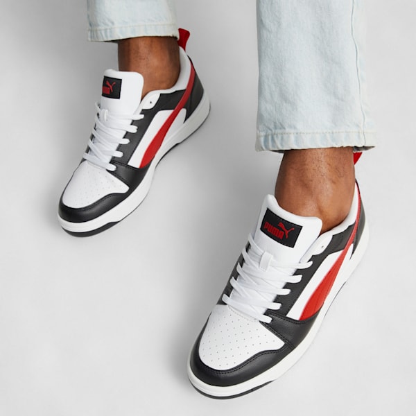 On white, a person wears white, black, and red trainers with light blue jeans.
