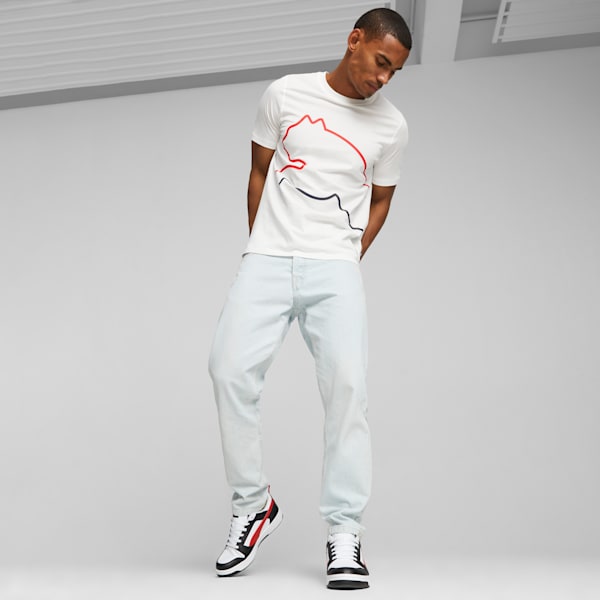 A model poses against a grey backdrop, wearing a printed tee, jeans and trainers.