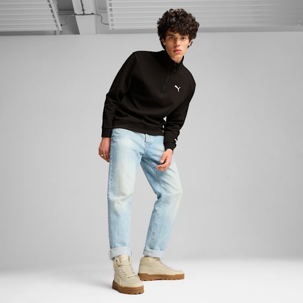 A model poses against a grey backdrop, wearing a black top, jeans, and boots.