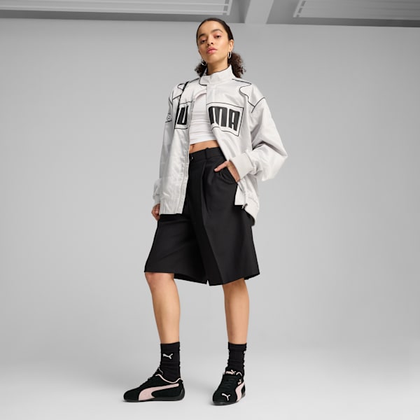 A model poses against a grey backdrop wearing a jacket, top, black shorts and trainers.