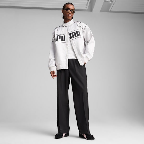 A model stands wearing a white jacket, t-shirt, black trousers, and shoes against a grey backdrop.