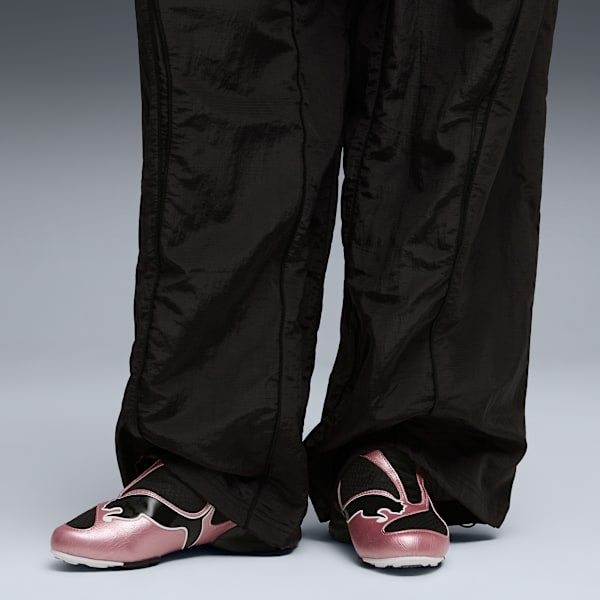 On grey, a model wears black trousers and pink trainers with a black logo.