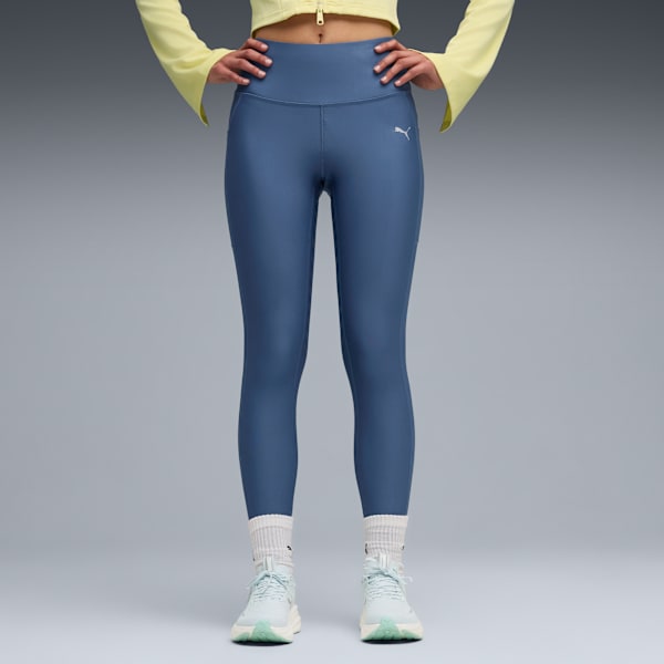A model stands against a grey backdrop wearing blue leggings, trainers and white socks.