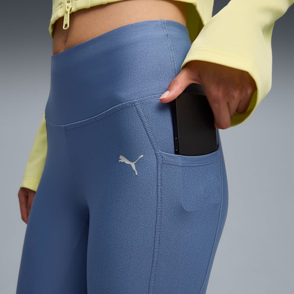 Against grey, a model puts a phone in the pocket of blue leggings.