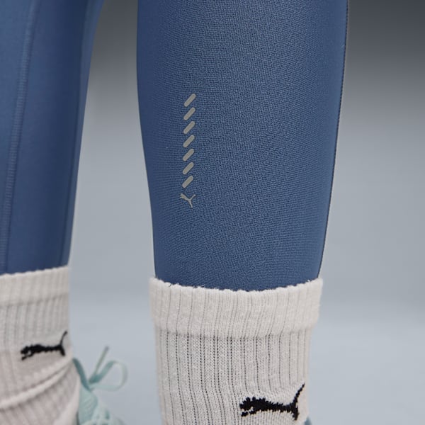 Legs wear blue leggings, Puma logo, and socks against a grey backdrop.