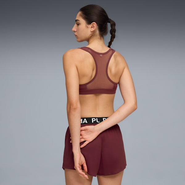 A model faces left against grey, wearing a maroon sports bra and shorts with a black waistband.