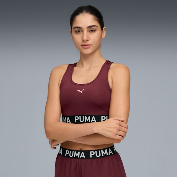 Against grey, a model poses with arms crossed wearing a maroon sports bra and matching bottoms.