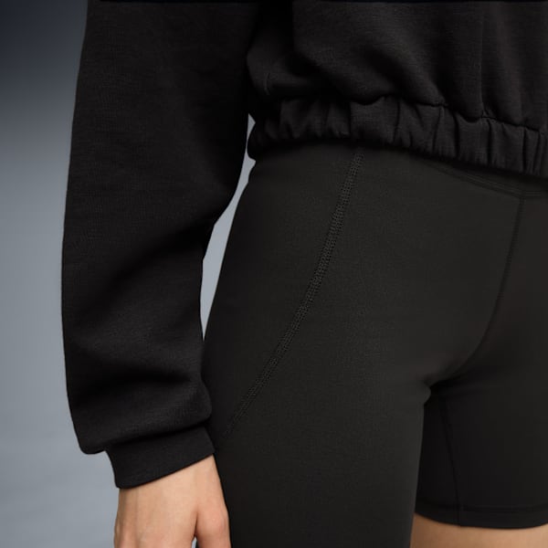 Against a grey backdrop, a model wears a black top and matching shorts.