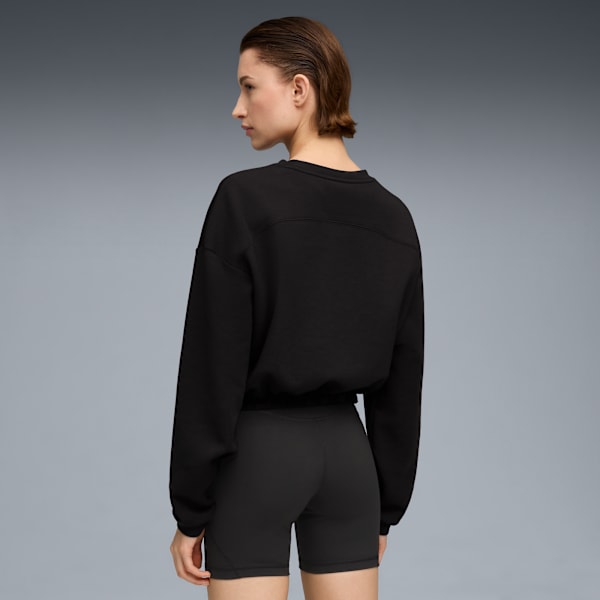 A model faces away against grey, wearing a black sweatshirt and black exercise shorts.