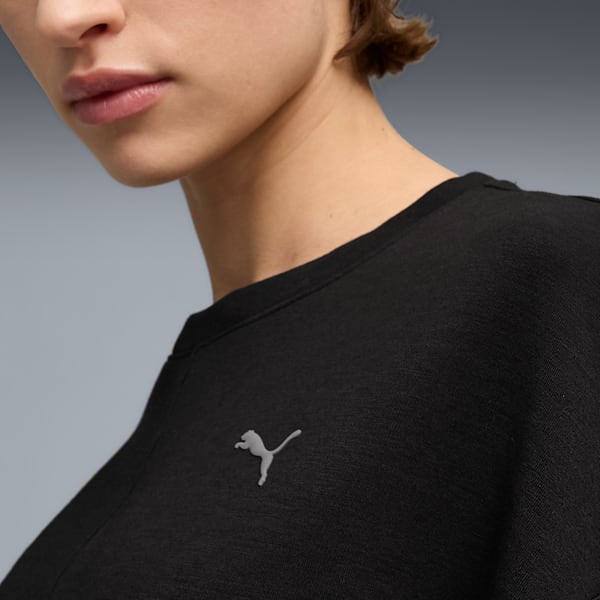 Close-up of a model wearing a black top featuring a brand logo against a grey backdrop.