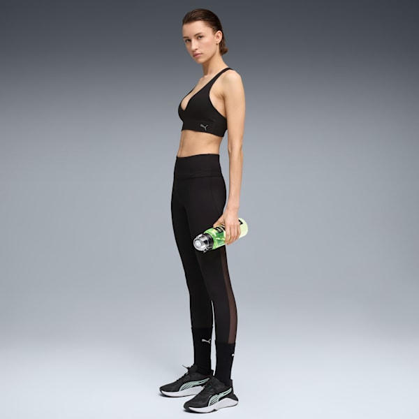 A model in black activewear holds a bottle against a grey backdrop, looking at the camera.