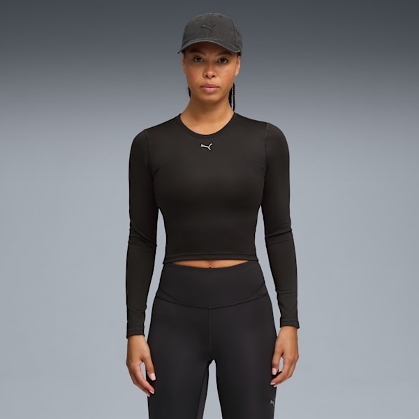 A model stands against grey, wearing a black long-sleeve top, leggings, and a cap.