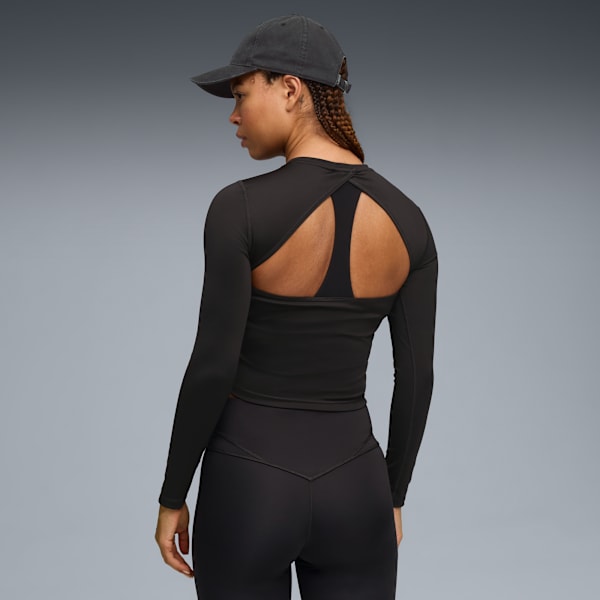 A model faces away on grey, wearing a black long-sleeve top, leggings and a cap.