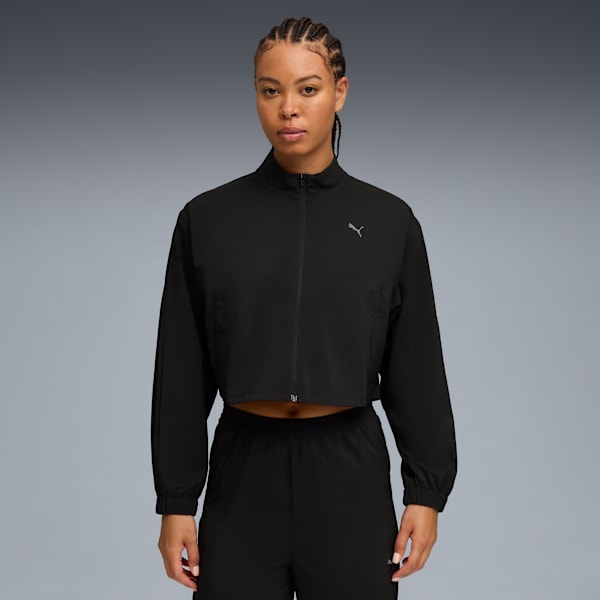 Against grey, a model poses in black activewear, featuring a zip-up jacket.