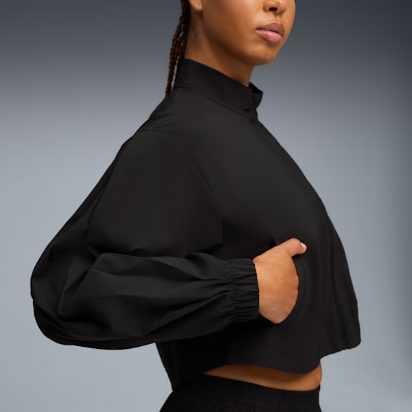 Against grey, a model poses in a black cropped jacket, hand in pocket.