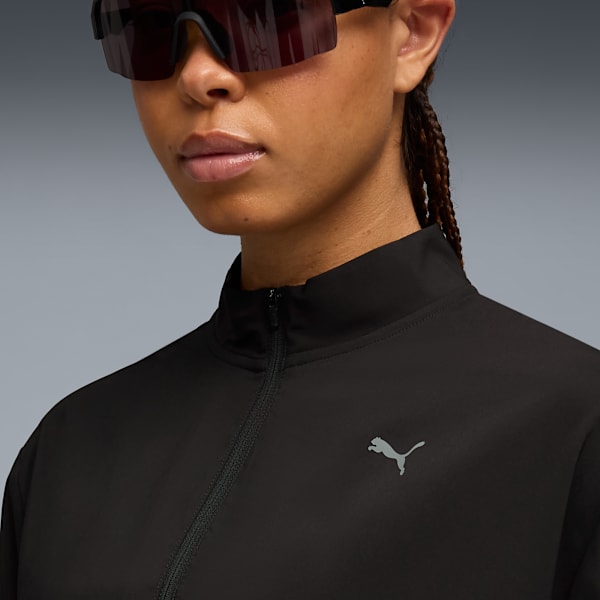 A model wears sunglasses and a zipped black top with a grey Puma logo against a grey backdrop.