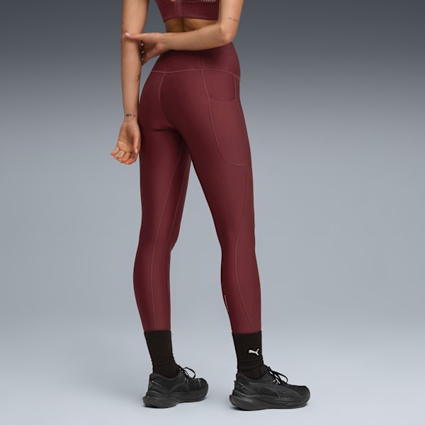 A model stands against grey, wearing maroon leggings, black socks and matching running shoes.