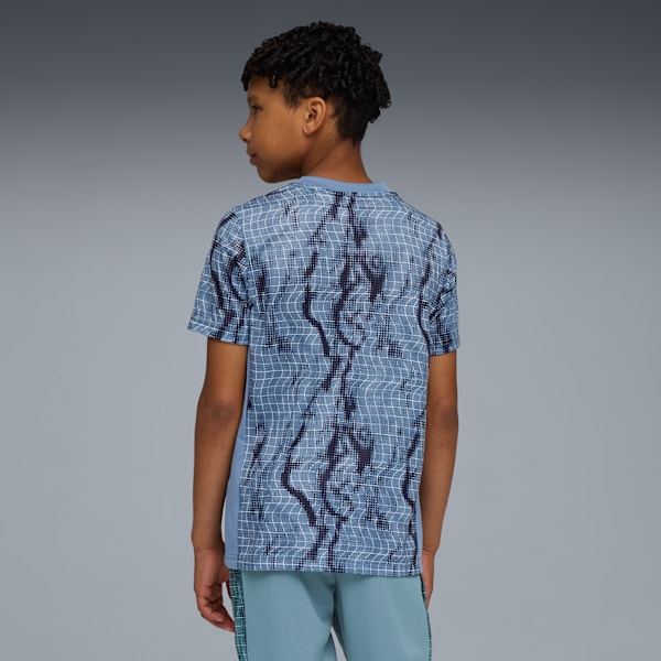 A model faces left against a grey background, wearing a patterned t-shirt and blue shorts.