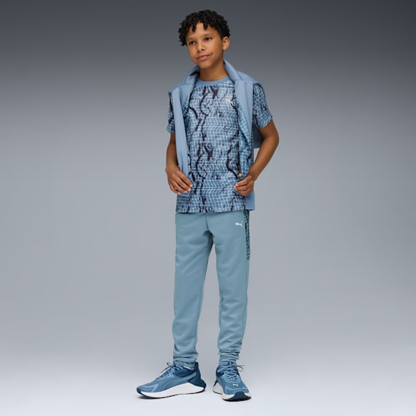 A model in front of a grey backdrop wearing a patterned t-shirt, trousers and trainers.