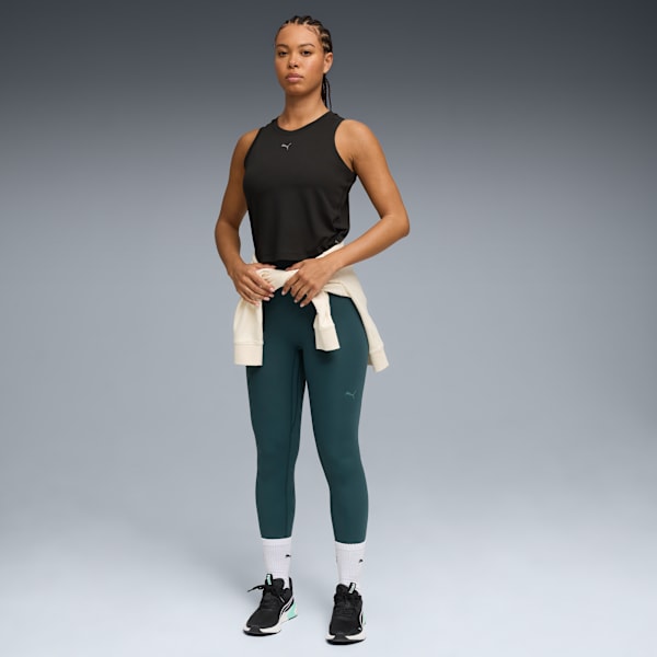 A model poses against grey, wearing a black top, leggings, trainers and a tied cream jumper.