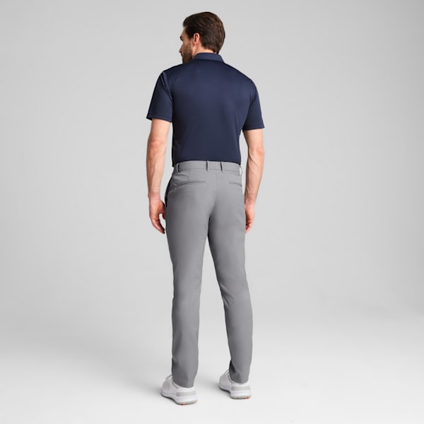 A model faces away on a grey background, wearing a dark polo shirt and grey trousers.