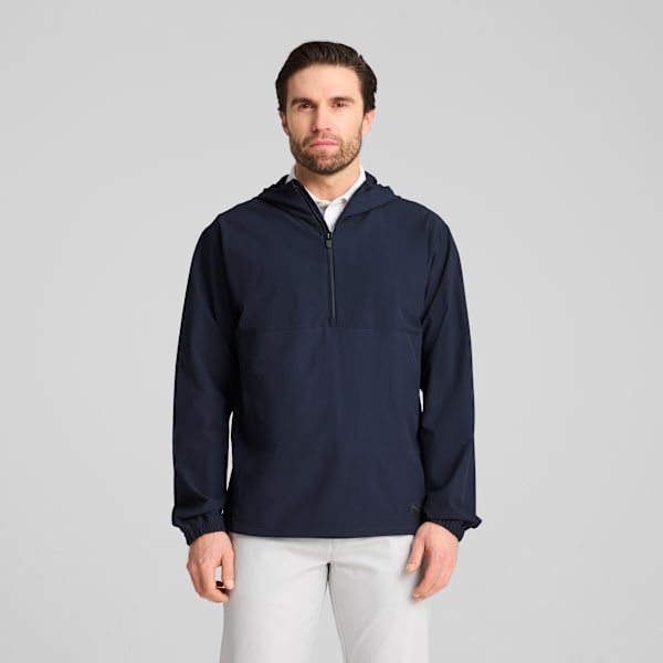 A model stands against a grey backdrop, wearing a navy hooded top and light trousers.