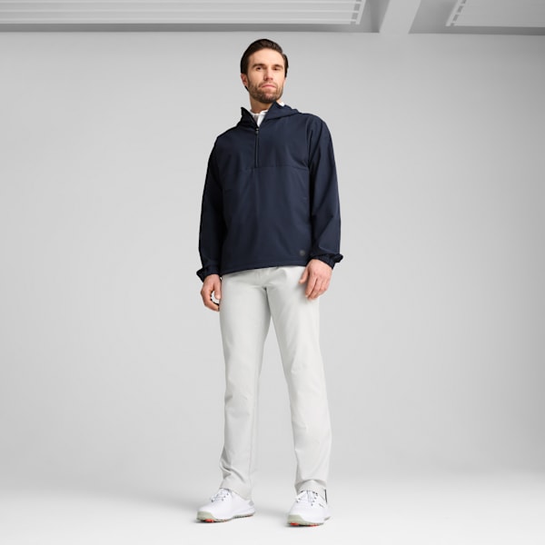 A model stands against a grey backdrop wearing a navy hooded top, light trousers and white shoes.