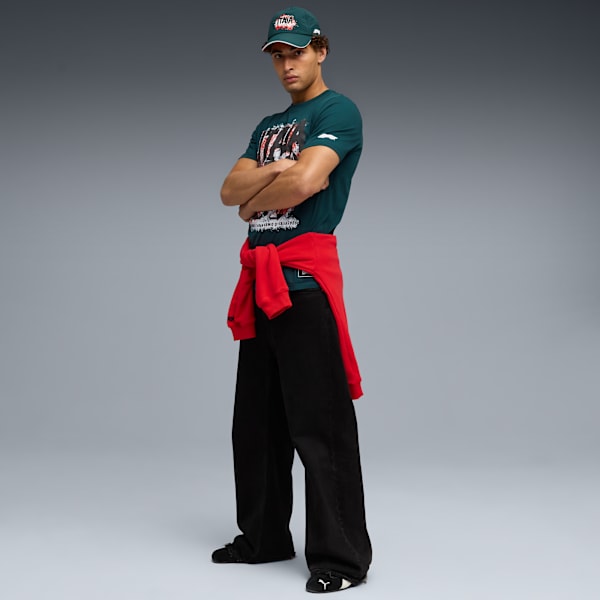 A model with crossed arms in front of a grey background wearing casual clothing.