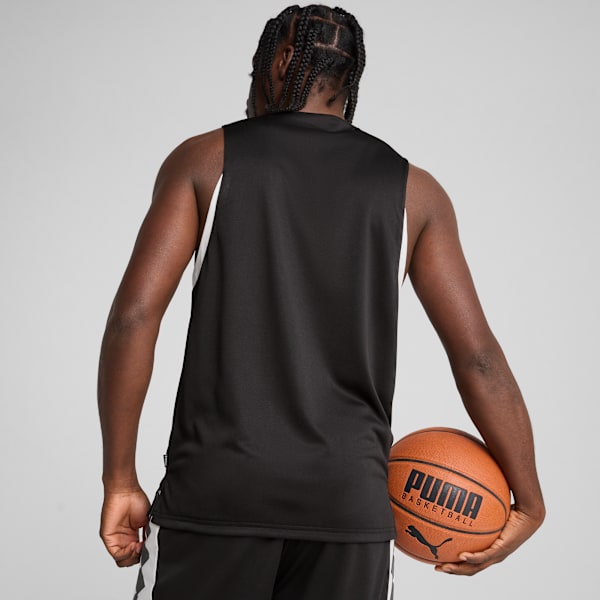 A model with braids faces away, holding a basketball against a grey backdrop.