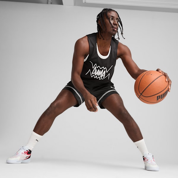 A model dribbles a basketball on a grey background, wearing a black Puma branded jersey.