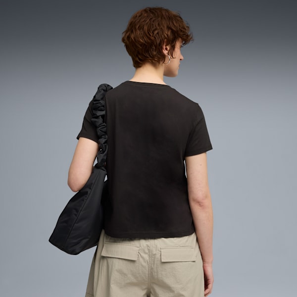 A model faces away against grey, wearing a dark t-shirt, light shorts and a black shoulder bag.