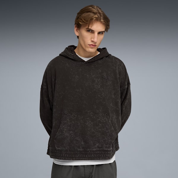A model poses against grey, wearing a dark hoodie and grey trousers.