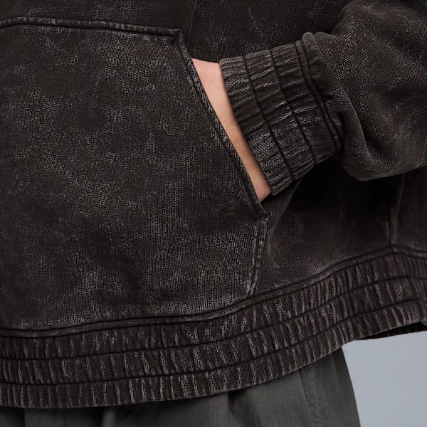 Close-up of a person's hand in the pocket of a black, textured hoodie against a neutral background.