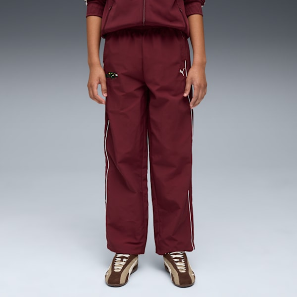 Against grey, a model wears maroon tracksuit bottoms and brown trainers.