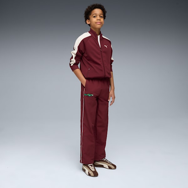 A model stands against a grey backdrop, wearing a maroon tracksuit with cream details.