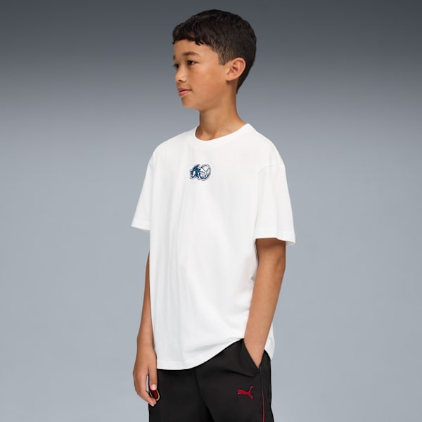 Against grey, a child models a white tee with a logo and black bottoms.