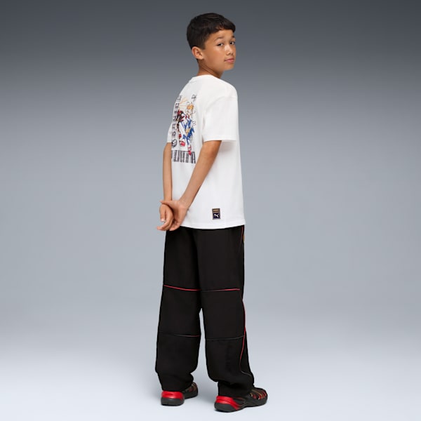 A model poses against a grey backdrop, wearing a graphic tee, black trousers and trainers.