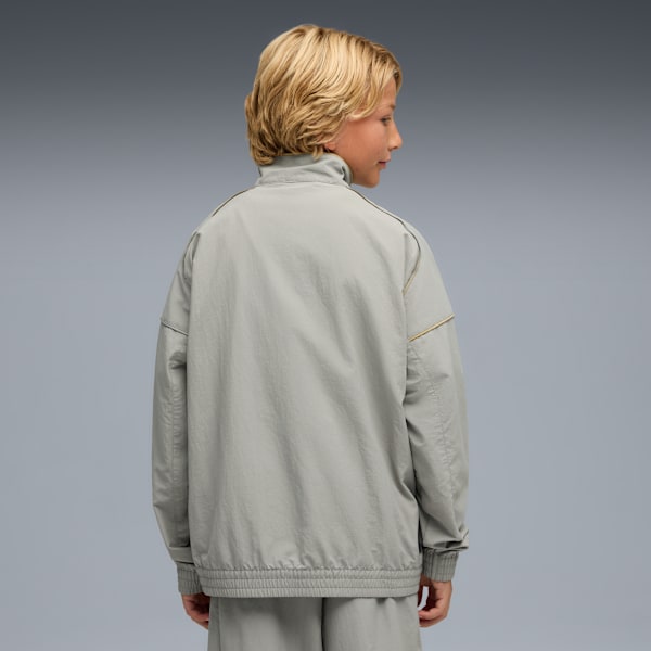 Seen from behind, a model poses against grey in a grey jacket and trousers.