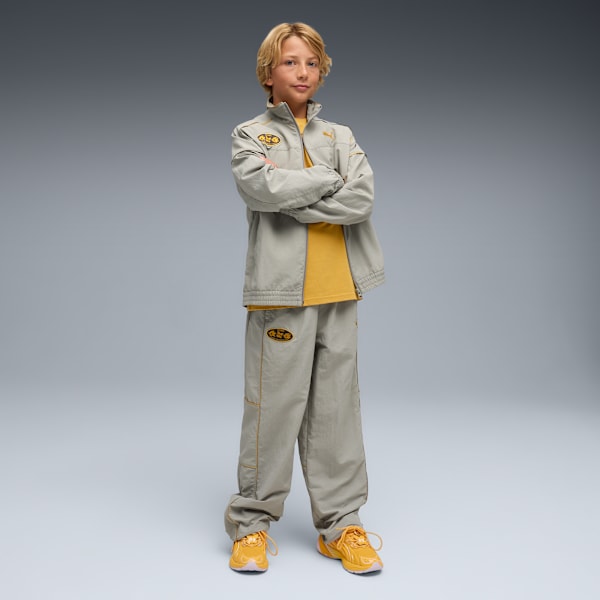 A child model stands with arms crossed against a grey backdrop, wearing a matching tracksuit.