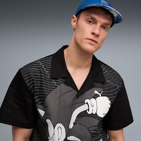 A model poses against a grey backdrop, wearing a graphic shirt and a blue cap.