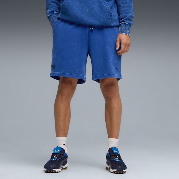 Against grey, a model wears blue shorts, a hoodie, white socks and patterned trainers.