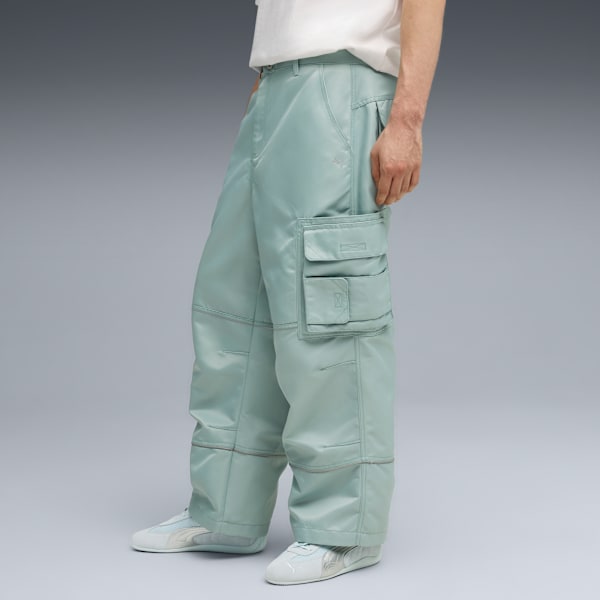 Against grey, a model is wearing light blue cargo trousers and trainers, hand in pocket.