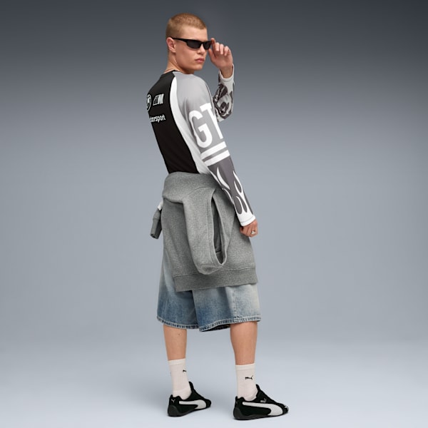 A model with sunglasses poses in front of a grey background wearing a motorsport shirt.