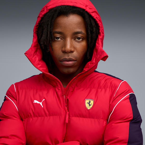 A model with dreadlocks poses in a red hooded jacket against a grey backdrop.