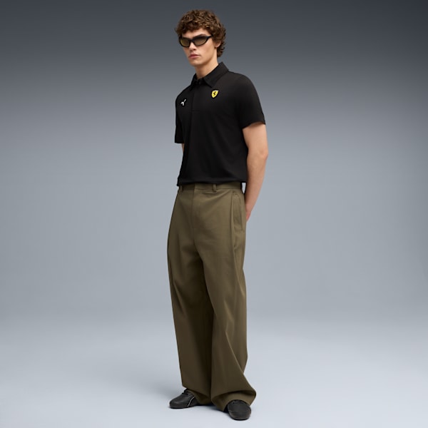 A model poses against a grey backdrop, wearing sunglasses, a black polo shirt, and olive trousers.