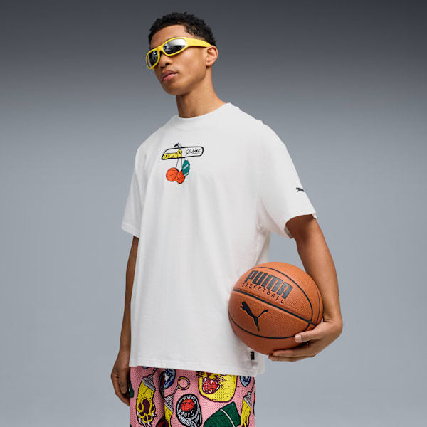 Against a grey backdrop, a model holds a basketball wearing a graphic tee and patterned shorts.