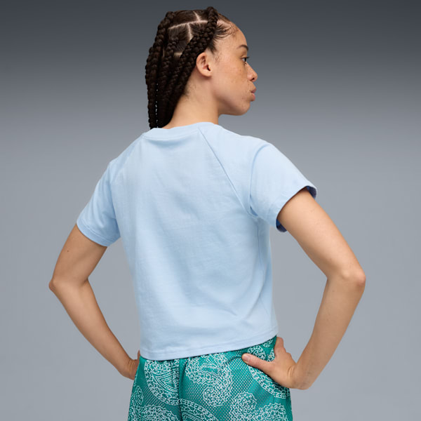 Against grey, a model poses in a light blue t-shirt and patterned teal shorts.