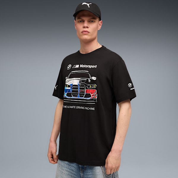 A model in front of a grey background wearing a black t-shirt and a black cap.
