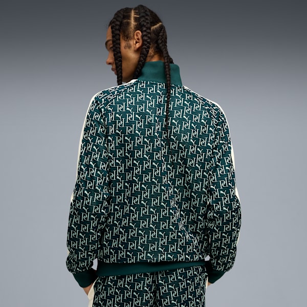 A model with braided hair poses against grey, wearing a patterned green jacket and matching trousers.