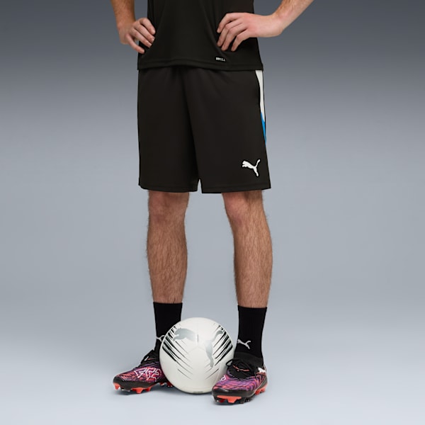 A model stands with a football, wearing black shorts, socks, and multi-coloured football boots.